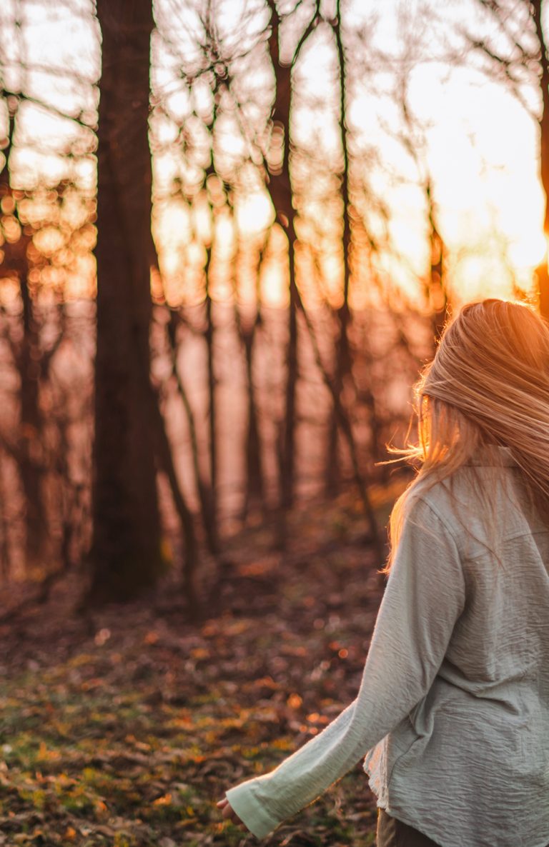 Vrouw in een herfstbos bij ondergaande zon